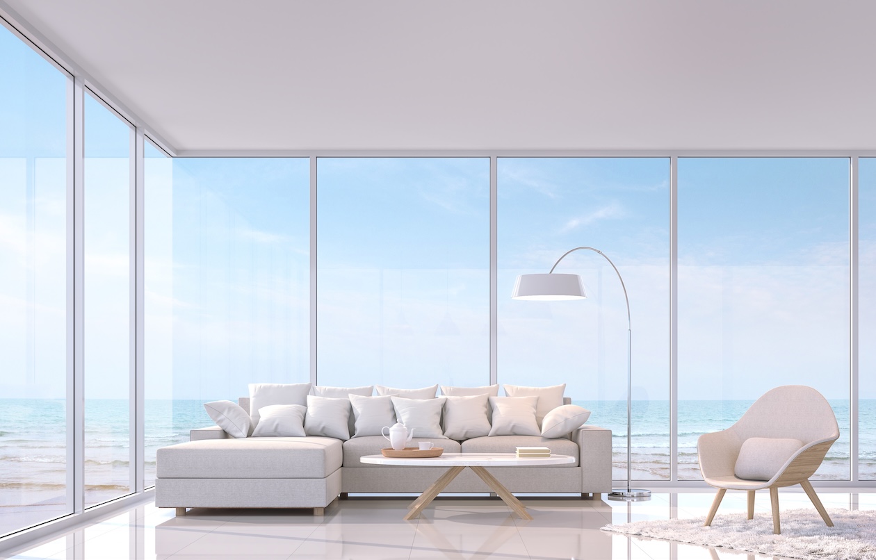 Modern white coastal living room with floor-to-ceiling windows and ocean view, featuring minimalist furniture and finishes designed for bright, sun-exposed coastal interiors.