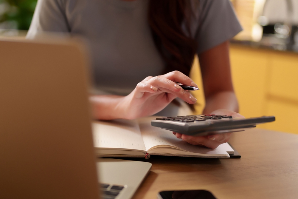 Calculator, notebook, and pen next to a laptop displaying a budgeting spreadsheet
