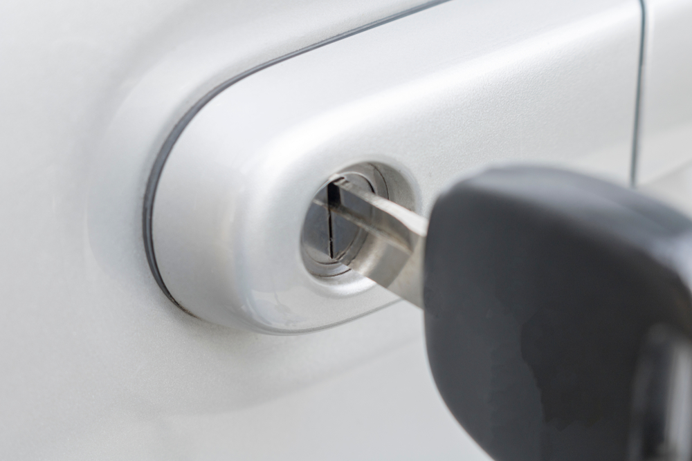 Locksmith unlocking a car door with specialised tools under the bright daylight